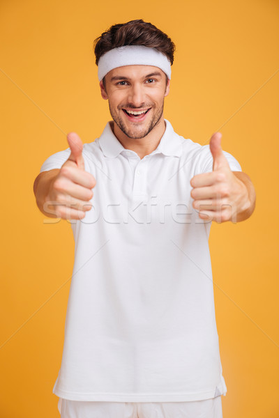 Cheerful handsome young sportsman showing thumbs up with both hands Stock photo © deandrobot