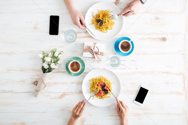Hands of young couple eating pasta together on wooden table Stock photo © deandrobot