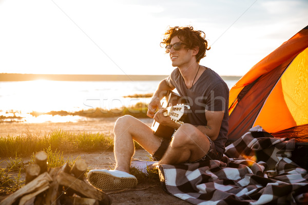 Smiling man sitting near touristic tent and playing guitar Stock photo © deandrobot