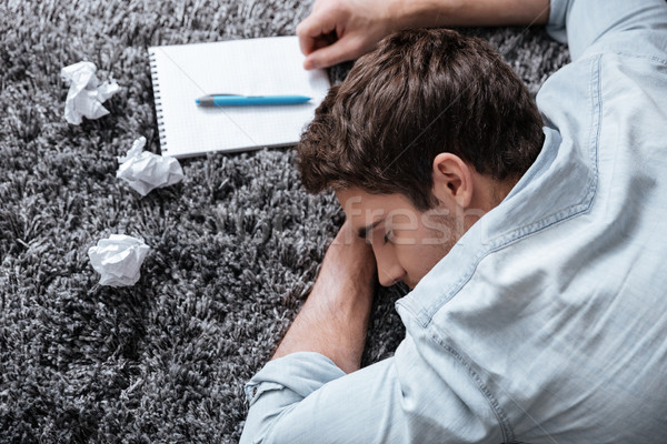 Young man sleeping on a carpet with notepad Stock photo © deandrobot