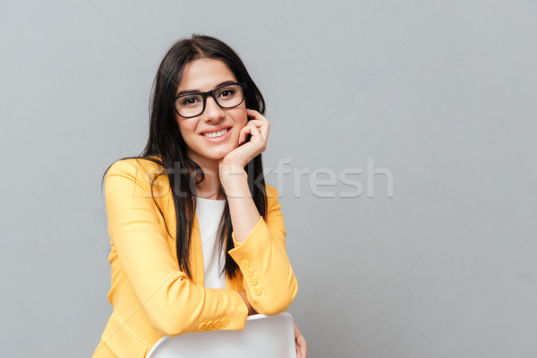 Charming lady sitting over grey background while looking to camera Stock photo © deandrobot