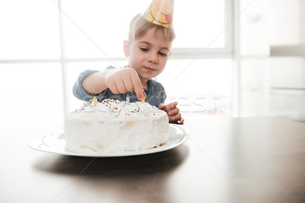 Cute birthday boy sitting in kitchen near cake. Stock photo © deandrobot