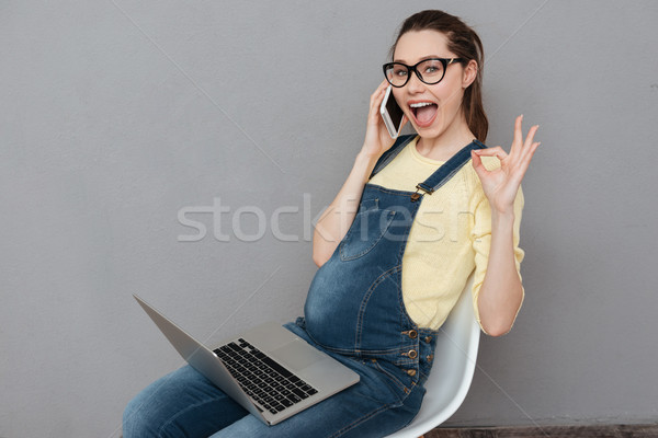 Pregnant happy lady talking by phone make okay gesture. Stock photo © deandrobot