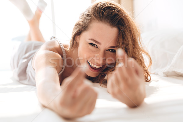 Smiling pretty lady lies in bed indoors calls you. Stock photo © deandrobot