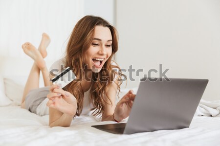 Happy woman with credit card and laptop sitting on sofa Stock photo © deandrobot