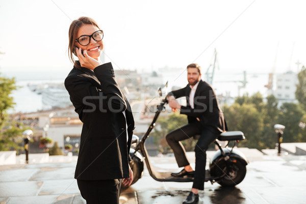 Joyful business woman posing outdoors and talking by smartphone Stock photo © deandrobot