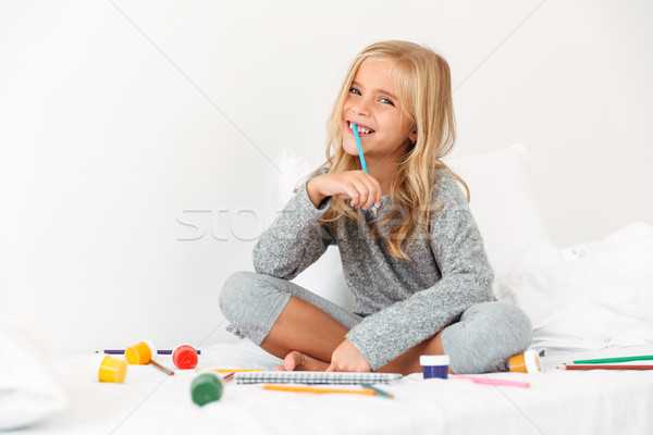 Happy blonde girl with pencil in her mouth sitting in bed, looki Stock photo © deandrobot