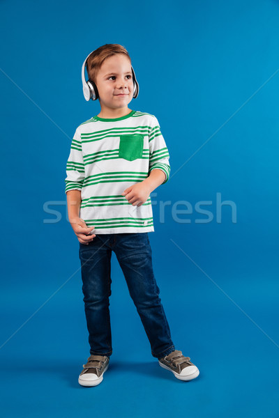 Full length image of cheerful young boy listening music Stock photo © deandrobot