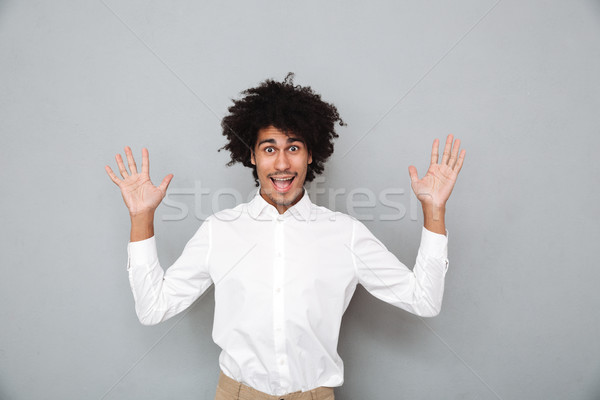 Portrait of a cheery young african man holding hands raised Stock photo © deandrobot