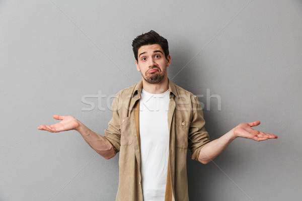 Portrait of a confused young casual shrugging shoulders Stock photo © deandrobot