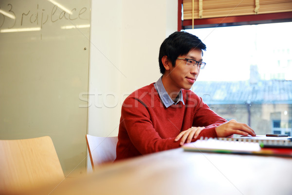 Young asian student in glasses sitting at the table Stock photo © deandrobot
