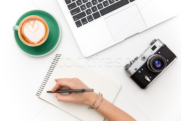 Laptop, camera, cup of coffee and hand writing in notebook Stock photo © deandrobot