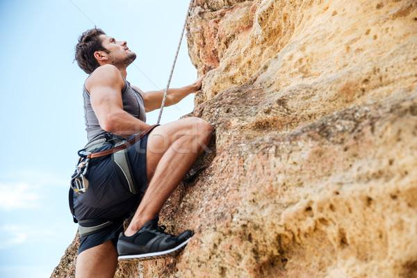 Young man climbing a steep wall in mountain Stock photo © deandrobot