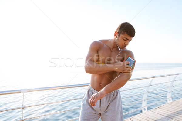 Serious african young sportsman using smartphone at the sea pier Stock photo © deandrobot