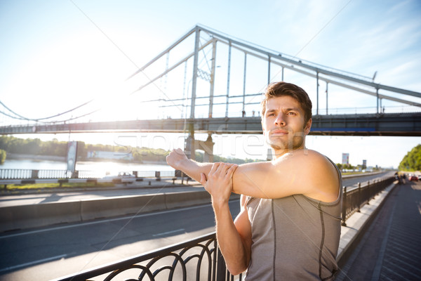 Sports man stretching at the bridge railing and looking away Stock photo © deandrobot