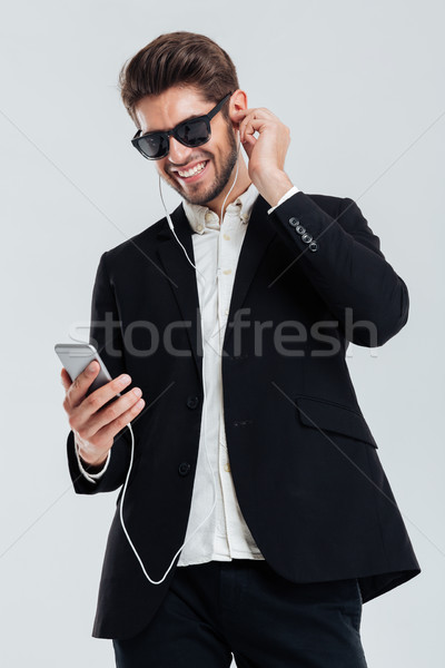 Smiling handsome young businessman listening music with earphones holding smartphone Stock photo © deandrobot