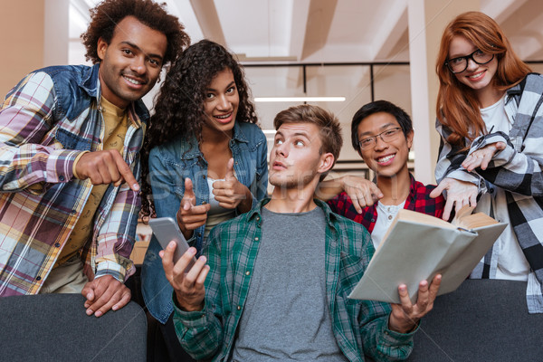 Cheerful young people pointing on student with book and smartphone Stock photo © deandrobot