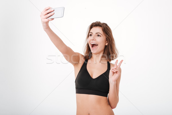 Fitness woman showing peace sign and taking selfie with smartphone Stock photo © deandrobot