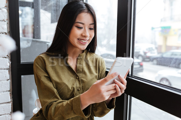 Pretty asian young lady chatting by her mobile phone. Stock photo © deandrobot