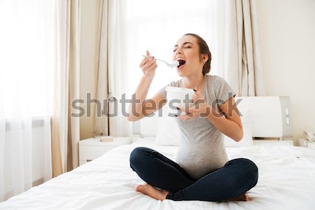 Cheerful pregnant young woman sitting and eating ice cream Stock photo © deandrobot