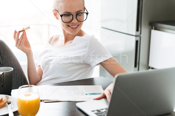 Cheerful lady eating bread with jam and using laptop Stock photo © deandrobot