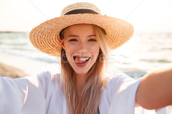 Photo of joyous blonde woman 20s in summer straw hat smiling, an Stock photo © deandrobot