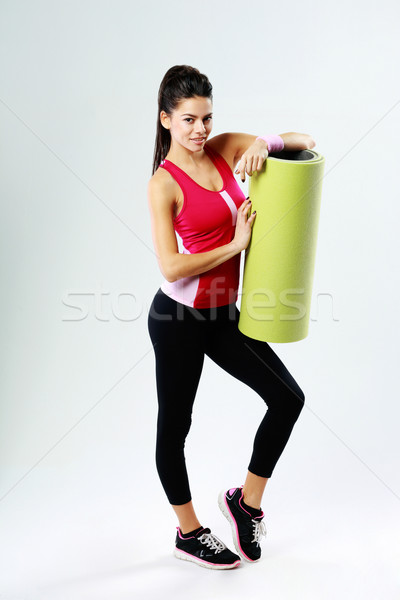 Full-length of a young sport woman with yoga mat on gray background Stock photo © deandrobot