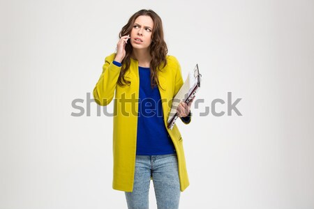 Thoughtful frowning young woman holding clipboard and using smartphone Stock photo © deandrobot