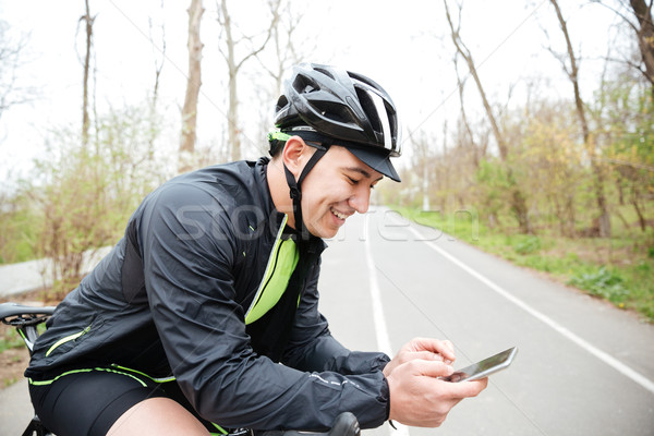 Cheerful young man with bicycle using mobile phone Stock photo © deandrobot