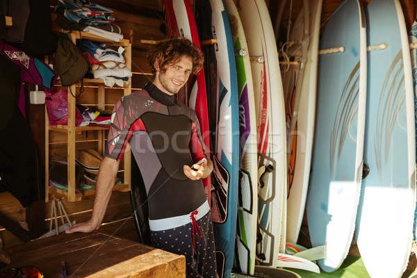 Om costum de baie smartphone în picioare surf zâmbitor Imagine de stoc © deandrobot