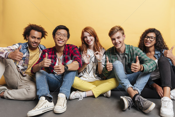 Multiethnic group of cheerful people sitting and showing thumbs up Stock photo © deandrobot