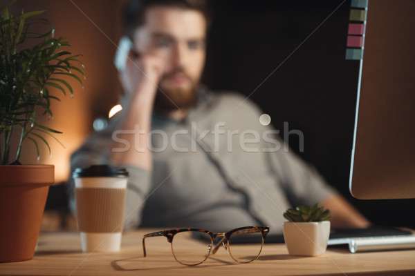 Designer working while talking by phone near glasses and coffee Stock photo © deandrobot