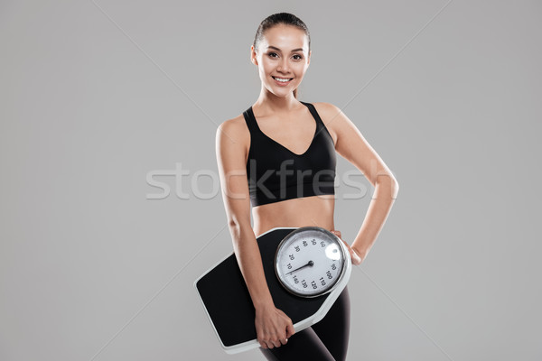 Cheerful attractive young woman athlete standing and holding weighing scale Stock photo © deandrobot