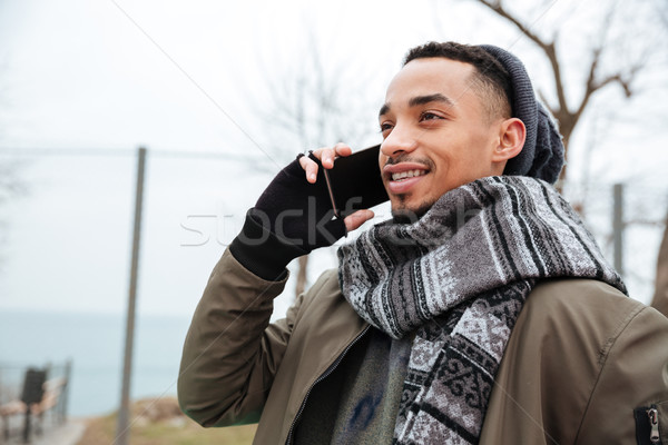 Smiling young african man talking by phone. Stock photo © deandrobot