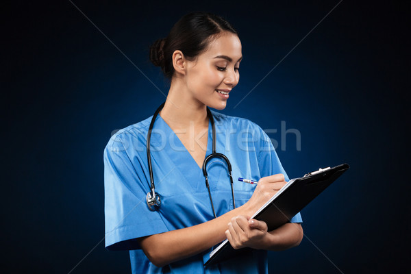 Young smiling doctor writing diagnosis in folder isolated Stock photo © deandrobot