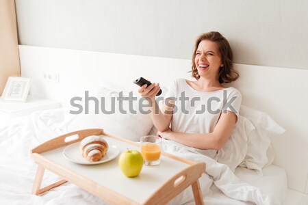 Stock photo: Cheerful young woman watch tv holding remote control.