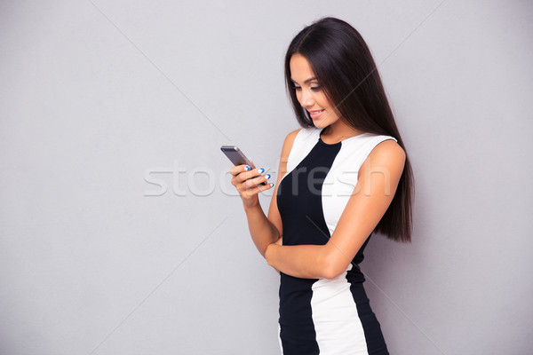 Сток-фото: улыбающаяся · женщина · платье · смартфон · портрет · серый · женщину