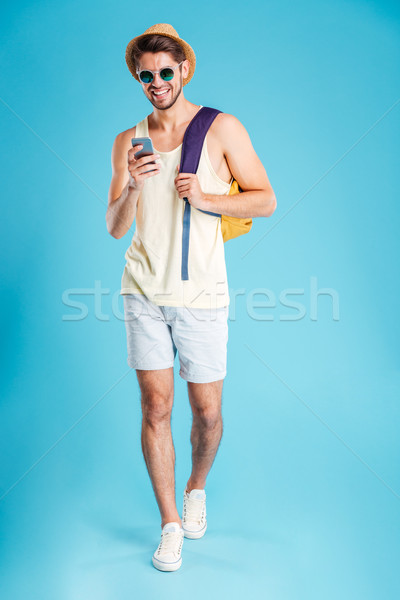 Smiling young man with backpack walking and using smartphone Stock photo © deandrobot