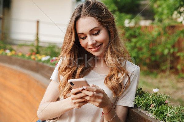 Stock photo: Smiling young girl in casual clothes using mobile phone