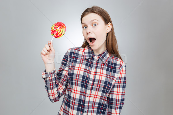 Amazed pretty teenage girl with mouth opened holding lollipop  Stock photo © deandrobot