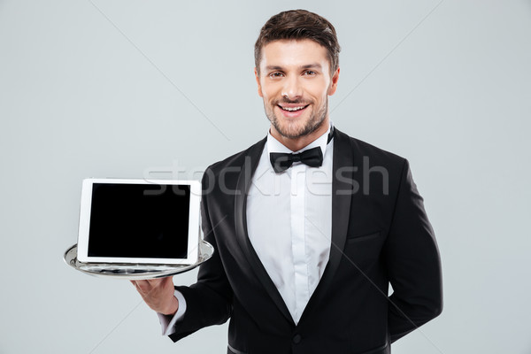 Cheerful waiter in tuxedo holding blank screen tablet on tray Stock photo © deandrobot