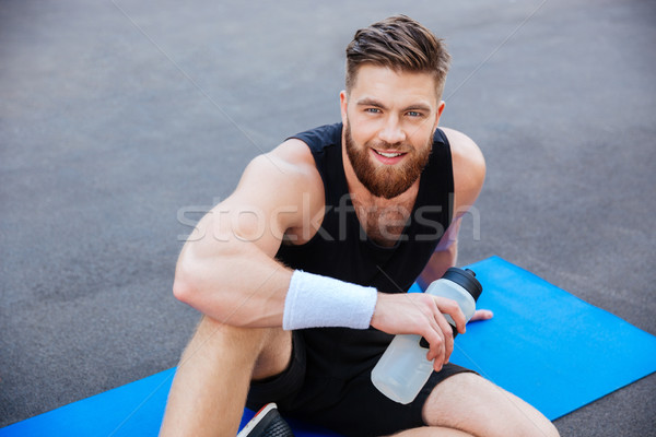 Smiling young sportsman with bottle of water relaxing outdoors Stock photo © deandrobot