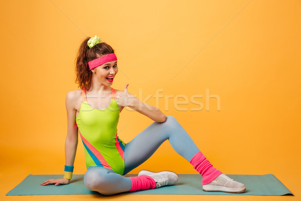 Cheerful woman athlete sitting on mat and showing thumbs up Stock photo © deandrobot