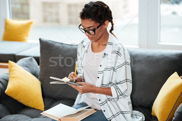 Attractive african lady wearing glasses writing notes. Stock photo © deandrobot