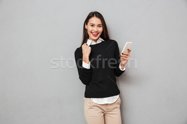 Happy asian woman in business clothes holding smartphone Stock photo © deandrobot