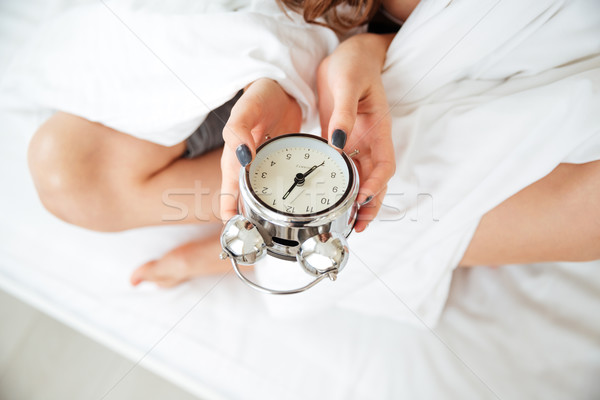 Stock photo: Female hands holding alarm clock on the bed