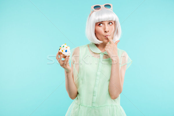 Funny blonde young woman standing and tasting cupcake by finger Stock photo © deandrobot