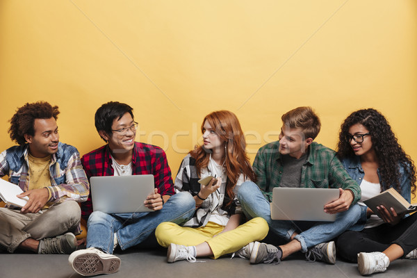 Cheerful people with laptop, book, smartphone sitting and talking Stock photo © deandrobot