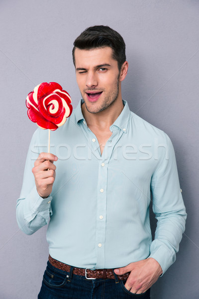 Young man holding lollipop and winking  Stock photo © deandrobot
