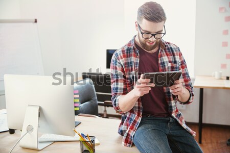 Cheerful young man sitting on the table and using smartphone Stock photo © deandrobot